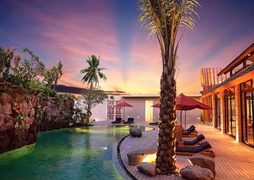 a swimming pool with chairs and palm trees next to a building at Maca Villas & Spa Bali in Seminyak