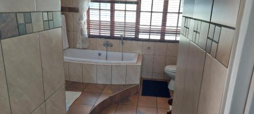a bathroom with a tub and a toilet and a window at 12 On Vaal Drive Guesthouse in Vanderbijlpark