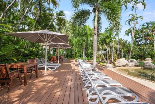 eine Holzterrasse mit Stühlen, Tischen und einem Sonnenschirm in der Unterkunft Reef Resort Villas Port Douglas in Port Douglas