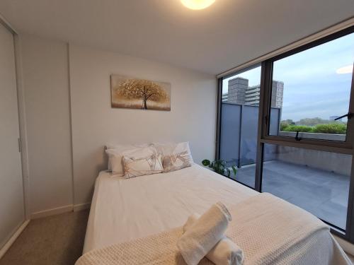 um quarto com uma cama e uma grande janela em Serenity 1br Flemington Balcony Pool Free Park em Melbourne