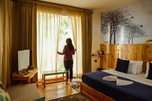 a woman looking out the window of a bedroom at Kasar Himalaya Holiday Resort, Binsar Rd in Almora