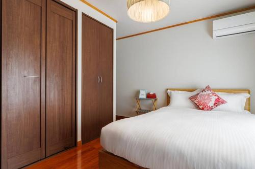 a bedroom with a white bed and a wooden cabinet at 恩納村飲食店の中心地ビーチまで徒歩3分最大12名貸切コーディアルステイ in Fuzuchi