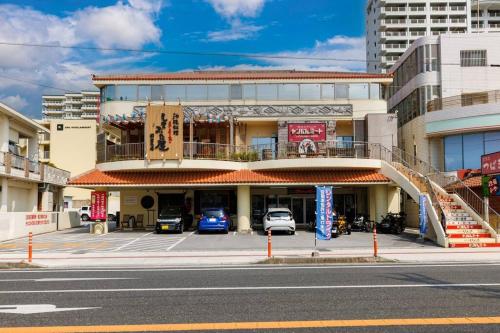a building with cars parked in a parking lot at 恩納村飲食店の中心地ビーチまで徒歩3分最大12名貸切コーディアルステイ in Fuzuchi