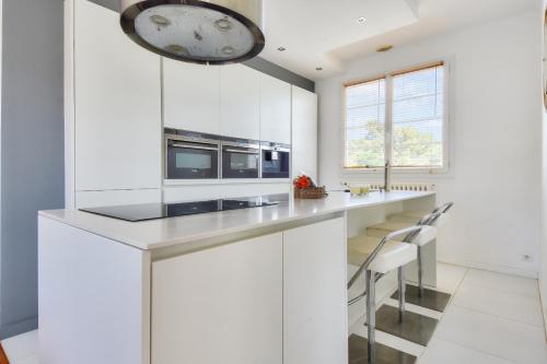 une cuisine avec des placards blancs et une horloge murale dans l'établissement Maison pour 10 avec piscine chauffée, à La Barre-de-Monts