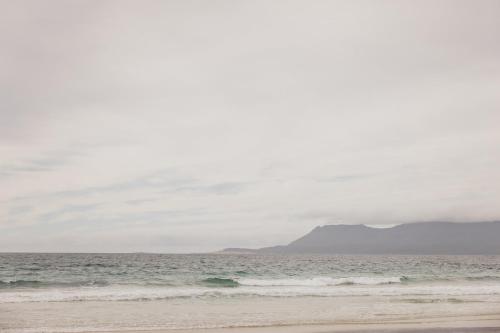 a beach with the ocean and a mountain in the background at 'Sisters' - Cliff top cabin with hot tub in Spring Beach