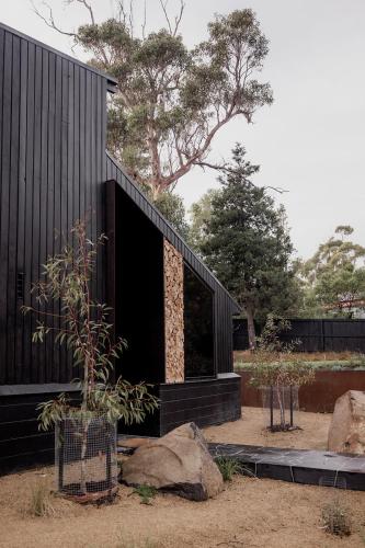 a black house with a tree and some rocks at 'Sisters' - Cliff top cabin with hot tub in Spring Beach