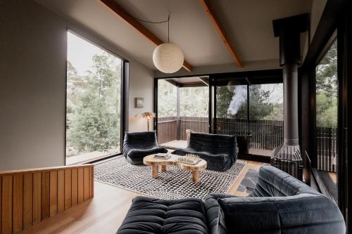 a living room with black furniture and large windows at 'Sisters' - Cliff top cabin with hot tub in Spring Beach