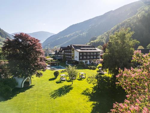 a building on a green field with mountains in the background at Familiengut Hotel Burgstaller in Döbriach