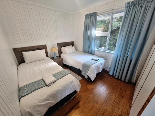 Un dormitorio con dos camas y una ventana con cortinas azules. en The Dunes Villa 11, en Plettenberg Bay