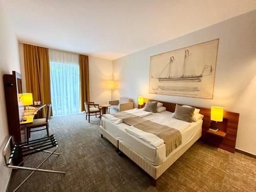ボニャルツバシュにあるZenit Wellness Hotel Balatonの大きなベッドとデスクが備わるホテルルームです。