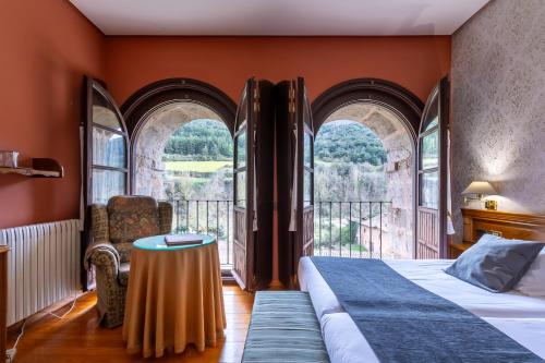 um quarto com uma cama com uma mesa e janelas em Hostería del Monasterio de San Millan em San Millán de la Cogolla