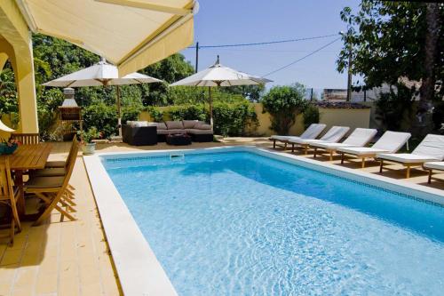 einen Pool mit einem Tisch, Stühlen und einem Sonnenschirm in der Unterkunft Villa Jasmim in Almancil