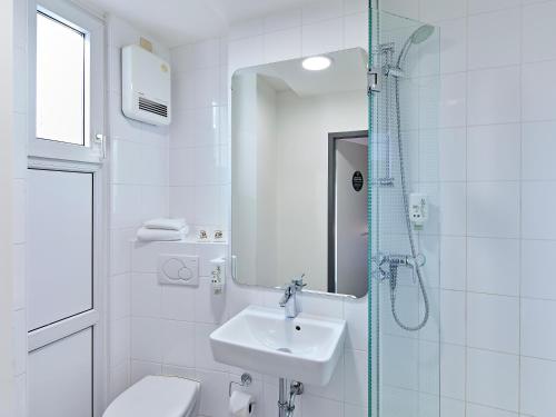a white bathroom with a sink and a shower at B&B Hotel Bonn-City in Bonn