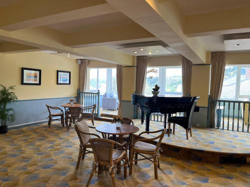 a room with a grand piano and tables and chairs at Biarritz Hotel in St Brelade