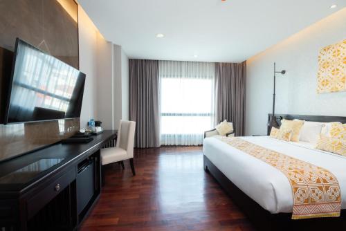 Habitación de hotel con cama, escritorio y TV. en Mintra Hotel en Vientián