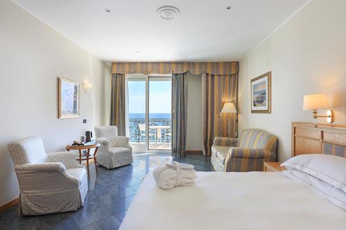 una habitación de hotel con una gran cama blanca y sillas en Grand Hotel Mediterranee, en Alassio