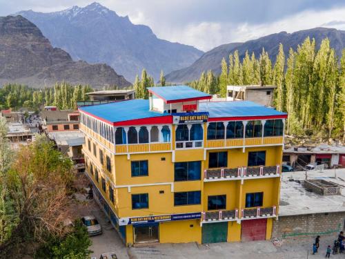 a yellow building with a blue roof with mountains in the background at Blue Sky Hotel & Restaurant in Skardu