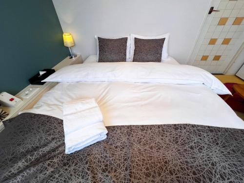 a large bed with white sheets and pillows at Hotel HAGOROMO in Hiroshima