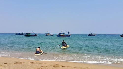two people on paddle boards in the ocean with boats at Homestay Beach View 2 in Phú Hiệp