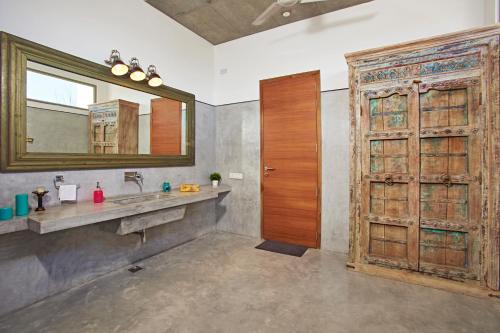baño con lavabo, espejo y puerta de madera en Manna Villa, en Mahabalipuram