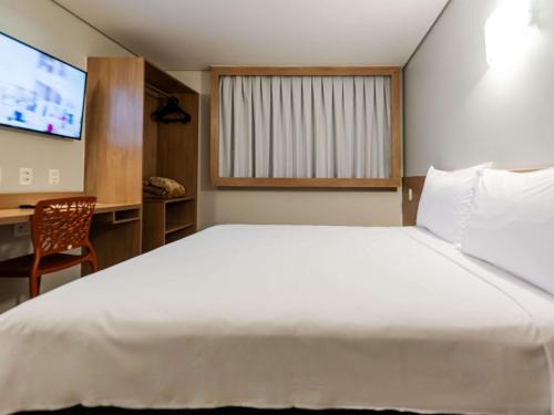 a bedroom with a large white bed and a television at ibis Styles Goiânia Shopping Estação in Goiânia