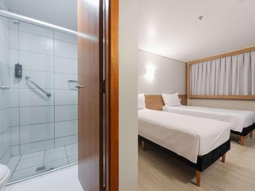 um quarto com 2 camas e uma cabina de duche em vidro em ibis Styles Goiânia Shopping Estação em Goiânia