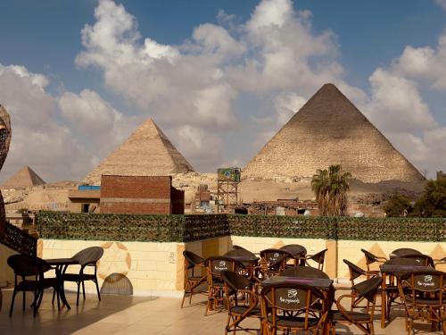 a patio with tables and chairs and pyramids in the background at Hur magic inn in Cairo