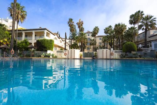 a large swimming pool with palm trees and buildings at Las Dunas Grand Luxury in Estepona