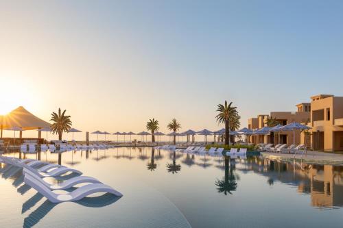 ラス・アル・ハイマにあるSofitel Al Hamra Beach Resortの白い椅子とヤシの木があるリゾートのプールを利用できます。