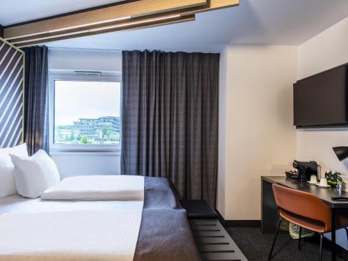 um quarto de hotel com uma cama, uma secretária e uma janela em B&B HOTEL München-Messe em Aschheim