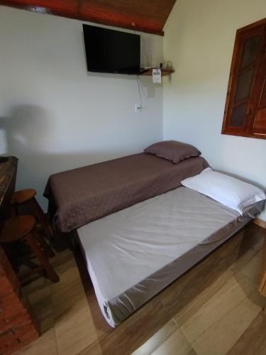 uma cama num quarto com uma televisão na parede em Chalé Pingo de Ouro em Alto Caparaó