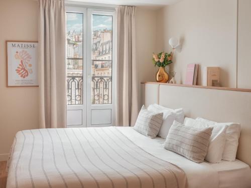 a bed with white sheets and pillows in front of a window at Hôtel Basss in Paris