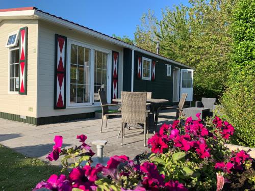 a house with a table and chairs and pink flowers at Chalet op vakantiepark in Baarland in Baarland