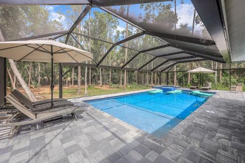 a swimming pool with an umbrella and two chairs at Luxury Family Pool, Jacuzzi, 2 Pickleball Court, Ping Pong Table Very Private Home Sleeps 8 in Naples
