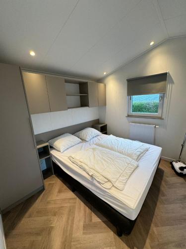 a bedroom with a large white bed with a window at Chalet op vakantiepark Molenhoek in Kamperland