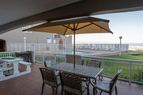 eine Terrasse mit einem Tisch, Stühlen und einem Sonnenschirm in der Unterkunft Jeffreys Bay Villas on The Beach in Jeffreys Bay