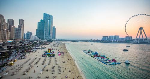 a beach with a bunch of people and a roller coaster at The W Jumeirah Beach in Dubai