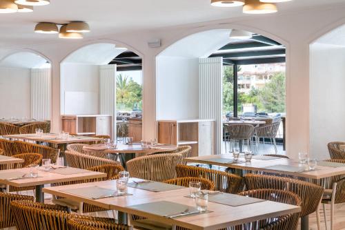 un restaurante con mesas y sillas de madera y ventanas en Salles Hotels Marina Portals, en Portals Nous