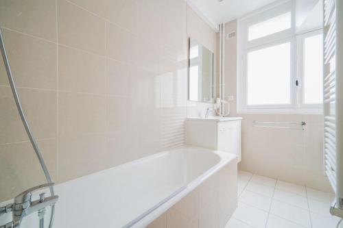 La salle de bains blanche est pourvue d'une baignoire et d'une fenêtre. dans l'établissement Appartement proche Fondation Louis Vuitton - III, à Neuilly-sur-Seine