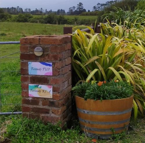 a brick box with signs on it next to plants at Taranaki Creekside TUI by Tiny Away in Stratford