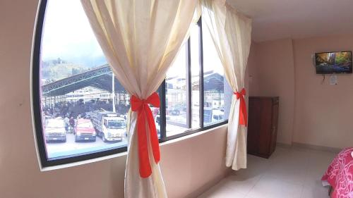 Habitación con una ventana con cortinas con arcos rojos en Hostal Flor de los Ángeles en Guamote