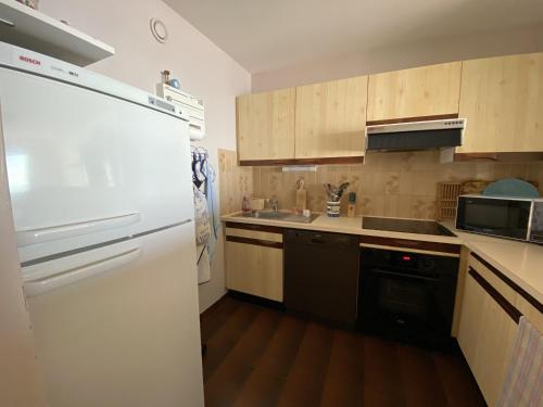 La cuisine est équipée d'un réfrigérateur blanc et de placards en bois. dans l'établissement Bel Appartement face mer - GARAGE, à Les Sables-dʼOlonne