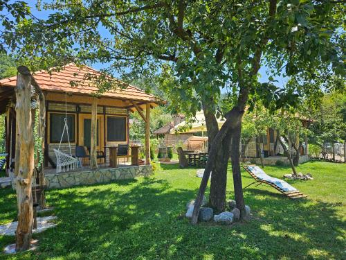 a house with a tree and a hammock in a yard at Drinska Dedovina in Gornja Trešnjica