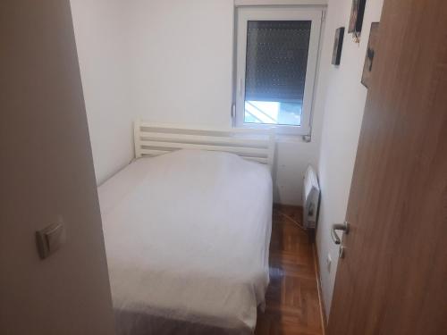 Un pequeño dormitorio con una cama blanca y una ventana en Leo en Surčin