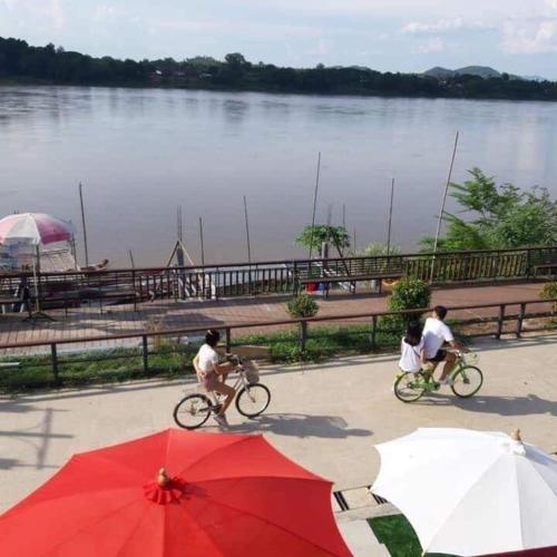a group of people riding bikes near a river with a red umbrella at บ้านสายน้ำ ติดแม่น้ำโขง in Chiang Khan