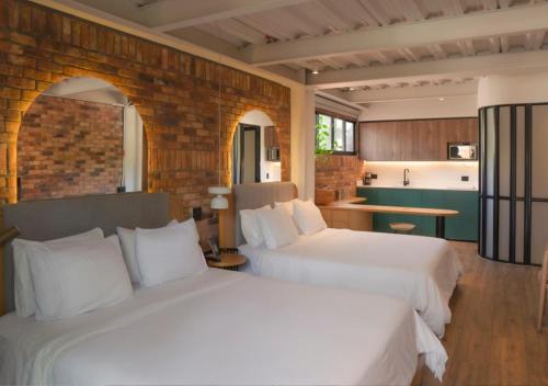 2 weiße Betten in einem Zimmer mit Küche in der Unterkunft Nomada Hotel Origen in Medellín