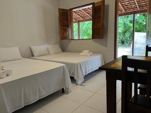 a room with two beds and a table and windows at POUSADA PARAÍSO CULTURAL in Barreirinhas