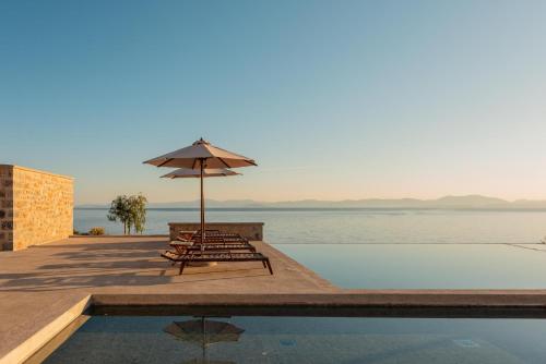 a pool with chairs and an umbrella next to the water at Sampatiki Suites & Spa - Luxury Seaview Suites - Opened 2024 in Leonidion