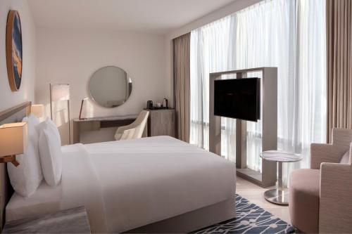 a white hotel room with a bed and a television at The First Collection Dubai Jumeirah Village Circle, a Tribute Portfolio Hotel in Dubai
