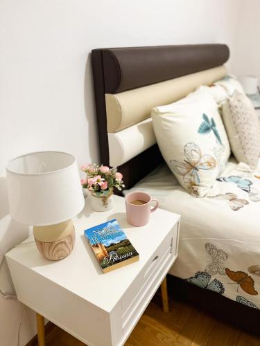 a bed with a table with a lamp and a book at Apartment Atria in Vrnjačka Banja